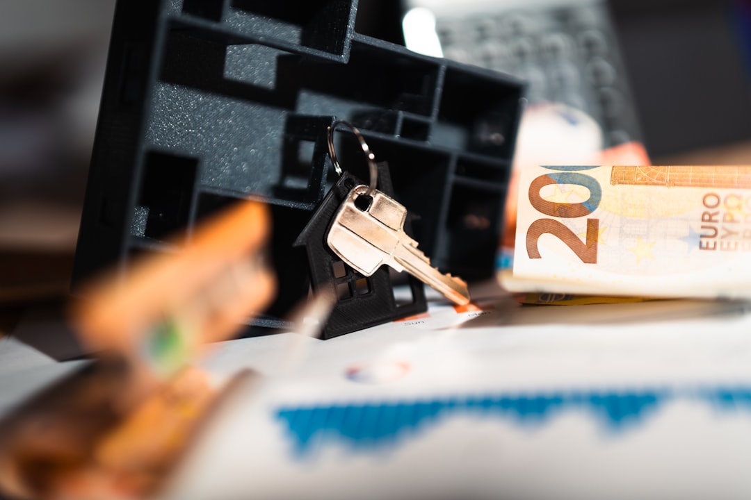 A person's hands use a calculator next to a set of house keys on a modern table, symbolizing the financial decisions of selling a home.